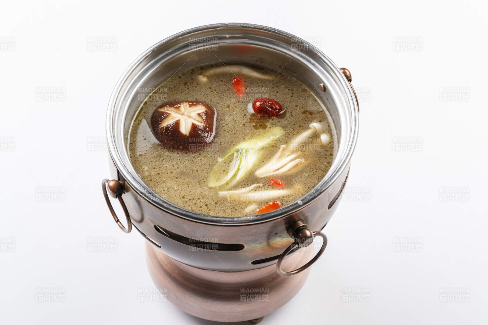 白色背景上的小火锅装的菌汤锅底图片