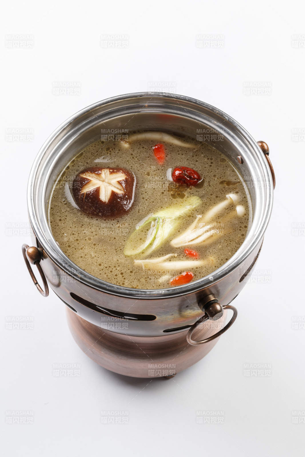 白色背景上的小火锅装的菌汤锅底图片