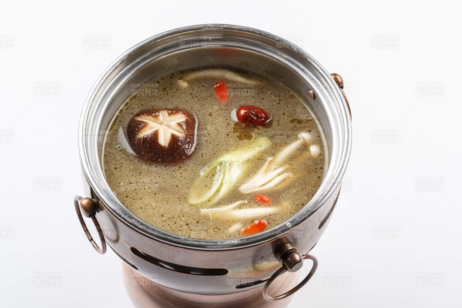 白色背景上的小火锅装的菌汤锅底图片