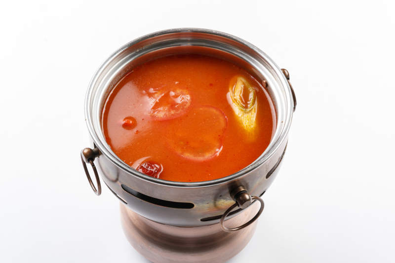 白色背景上的小火锅装的番茄锅底图片