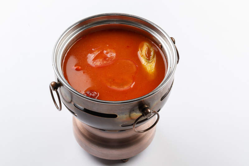 白色背景上的小火锅装的番茄锅底图片