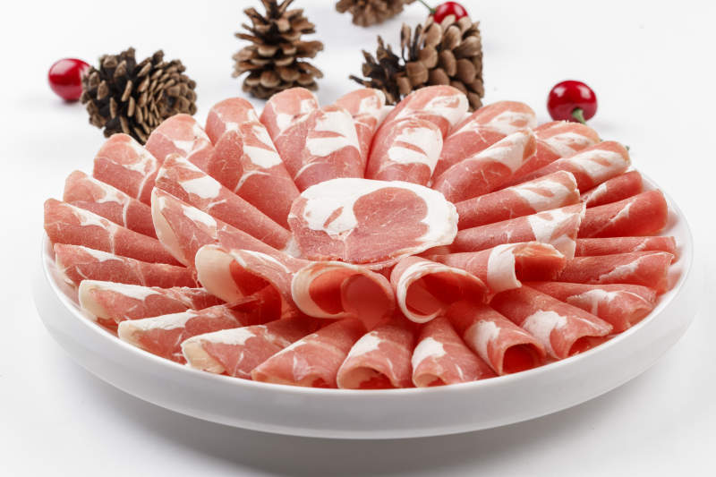 白色背景上的圆瓷盘装的涮锅食材肥牛片图片