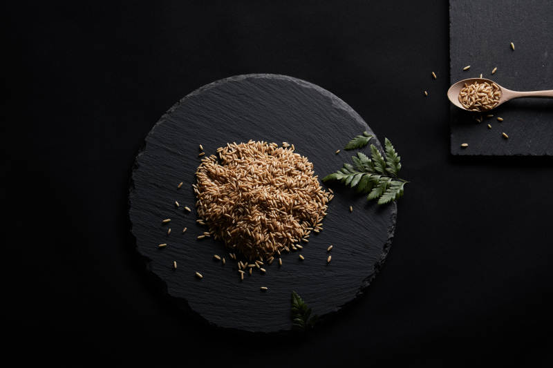 黑色青石板上的木质勺子装的燕麦米摆放在黑色背景中图片