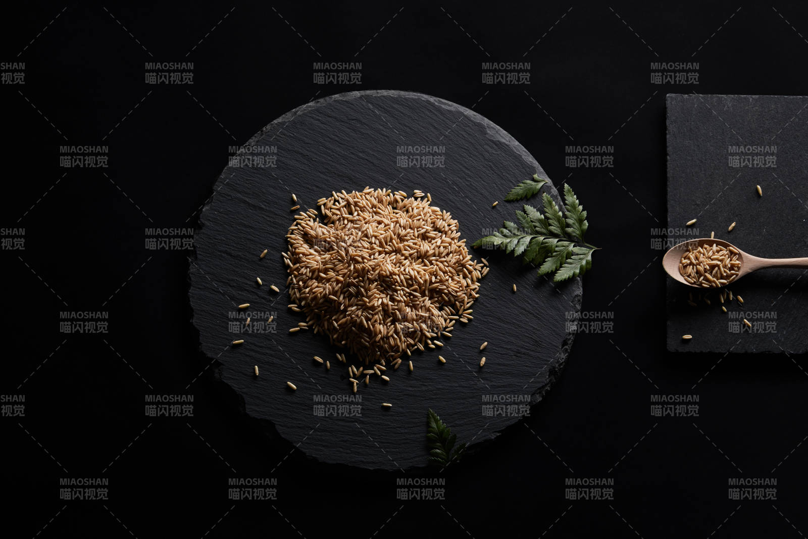 黑色青石板上的木质勺子装的燕麦米摆放在黑色背景中图片