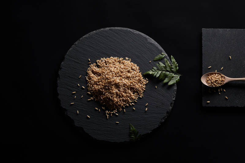 黑色青石板上的木质勺子装的燕麦米摆放在黑色背景中图片