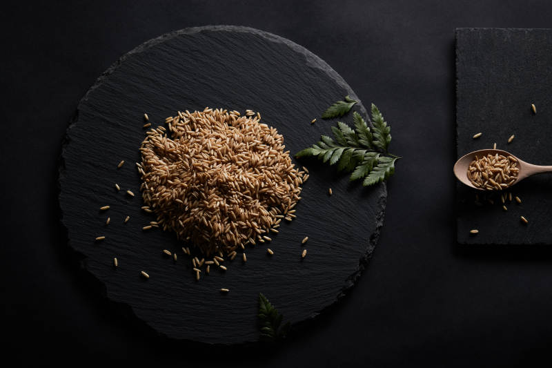 黑色青石板上的木质勺子装的燕麦米摆放在黑色背景中图片