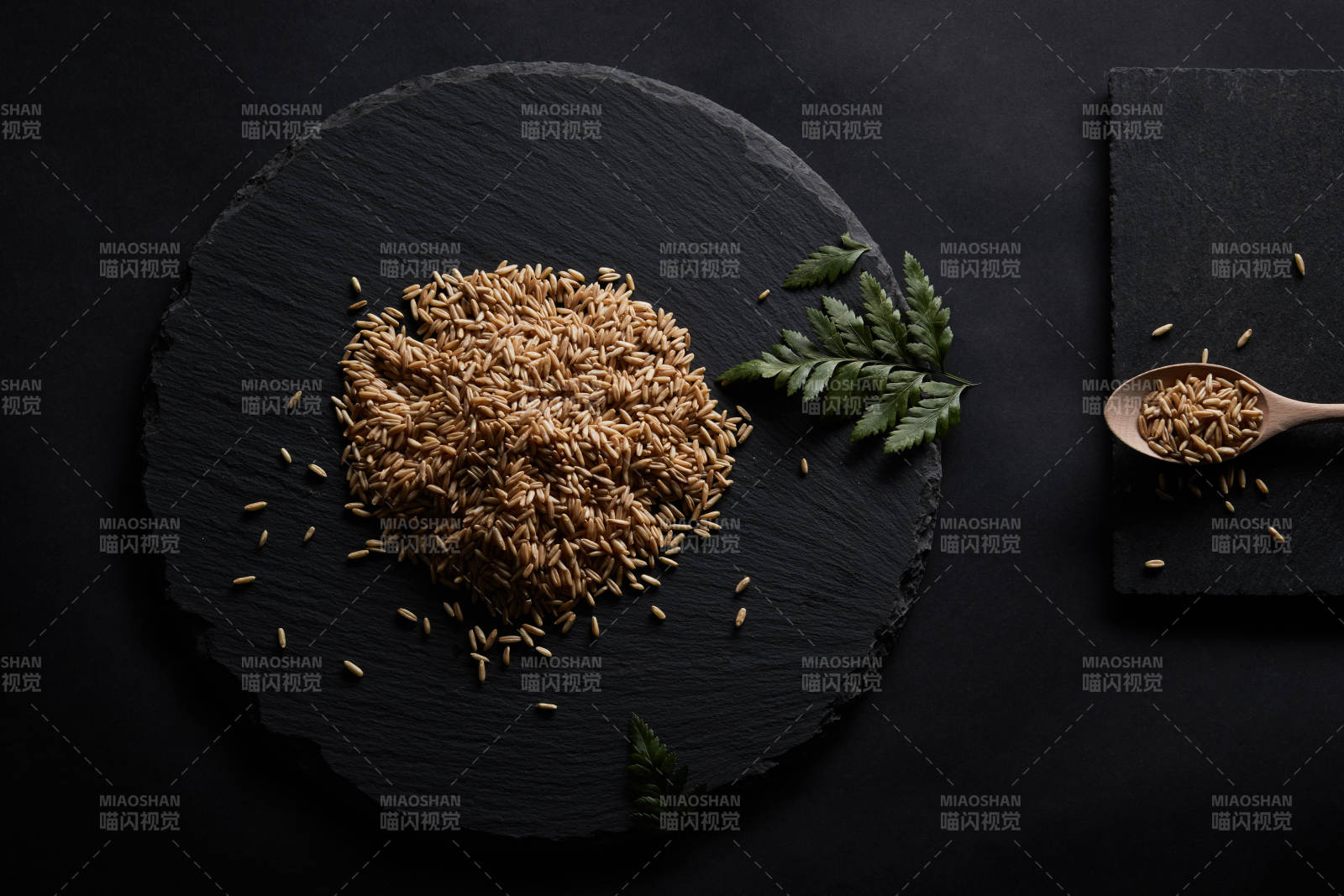 黑色青石板上的木质勺子装的燕麦米摆放在黑色背景中图片