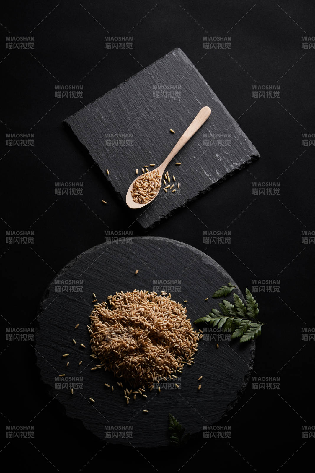 黑色青石板上的木质勺子装的燕麦米摆放在黑色背景中图片