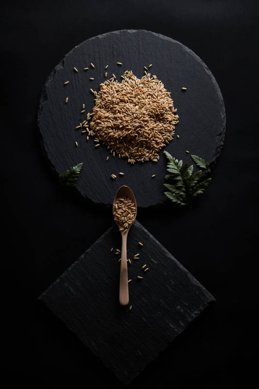 黑色青石板上的木质勺子装的燕麦米摆放在黑色背景中图片