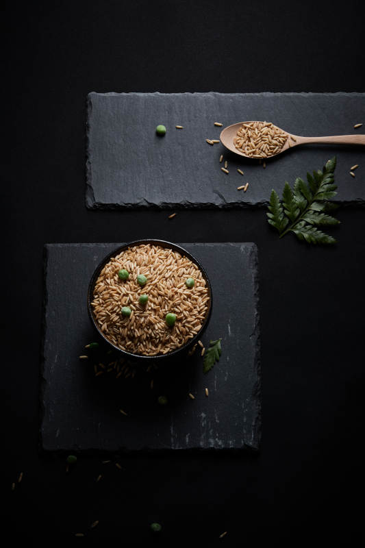 黑色青石板上的木质勺子装的燕麦米摆放在黑色背景中图片