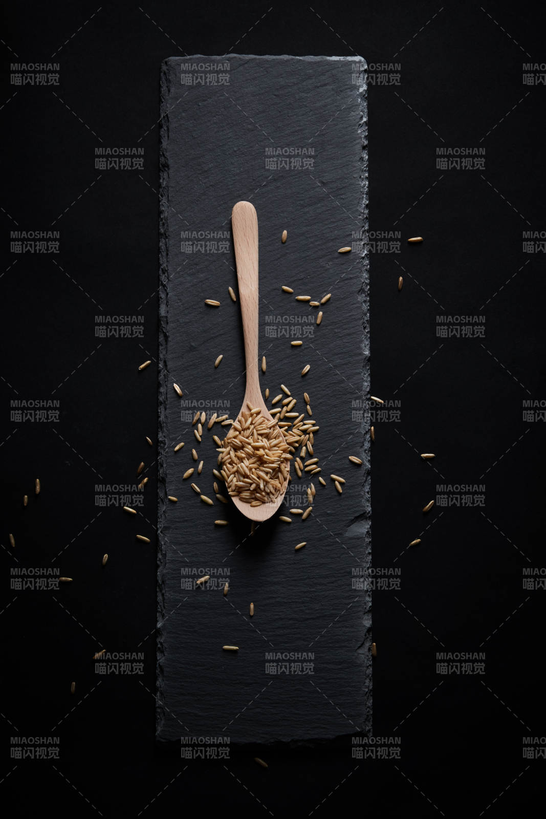 黑色青石板上的木质勺子装的燕麦米摆放在黑色背景中图片