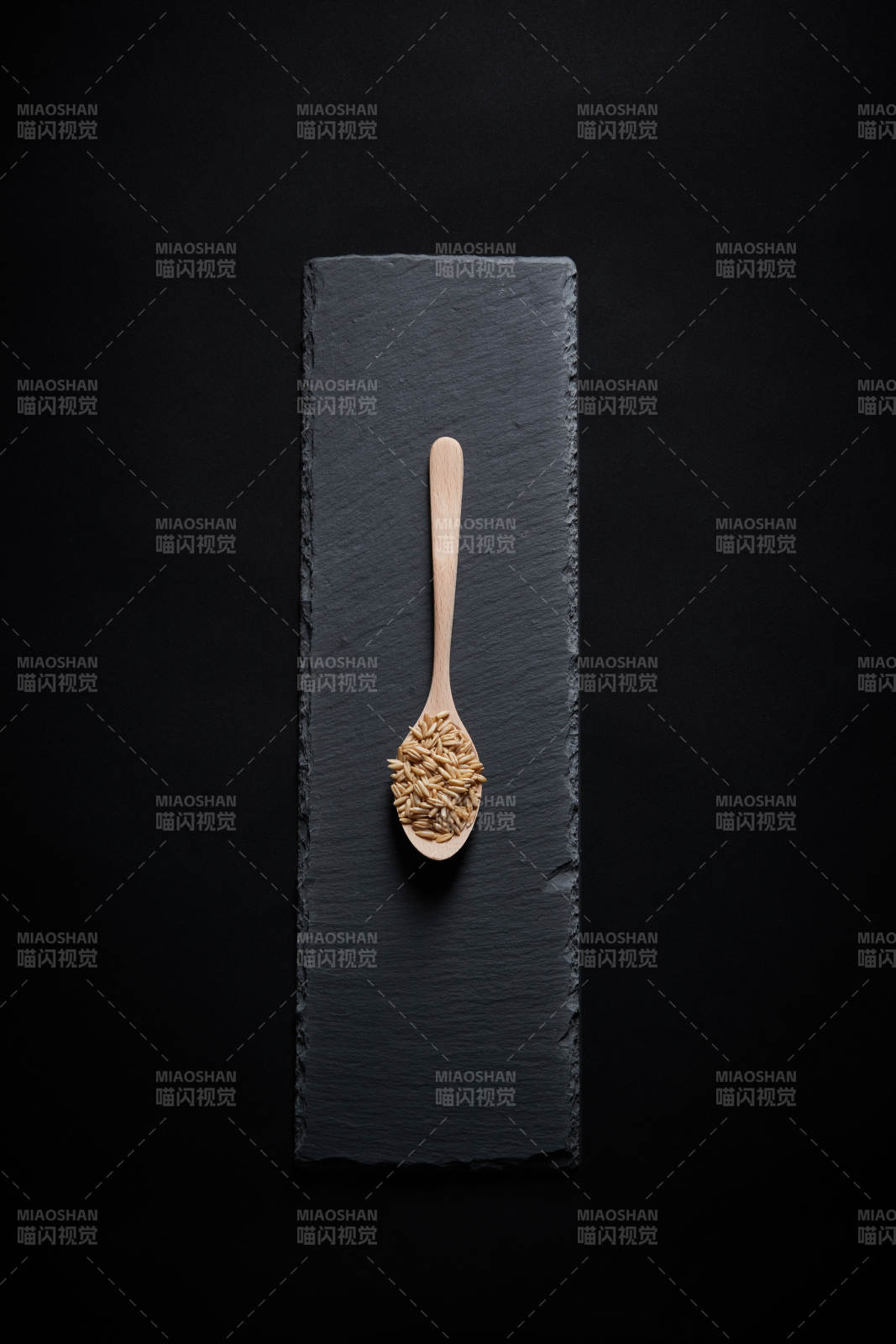 黑色青石板上的木质勺子装的燕麦米摆放在黑色背景中图片