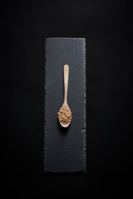 黑色青石板上的木质勺子装的燕麦米摆放在黑色背景中图片