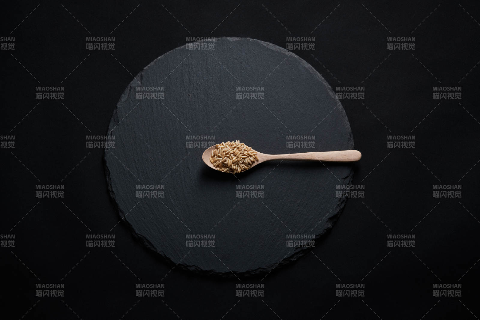 黑色青石板上的木质勺子装的燕麦米摆放在黑色背景中图片
