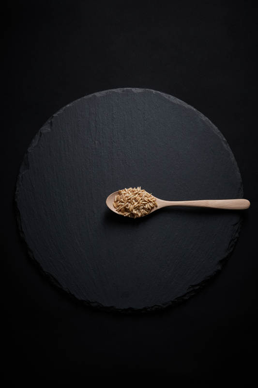 黑色青石板上的木质勺子装的燕麦米摆放在黑色背景中图片