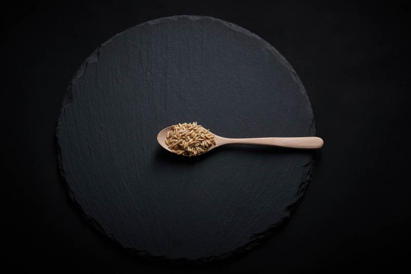 黑色青石板上的木质勺子装的燕麦米摆放在黑色背景中图片