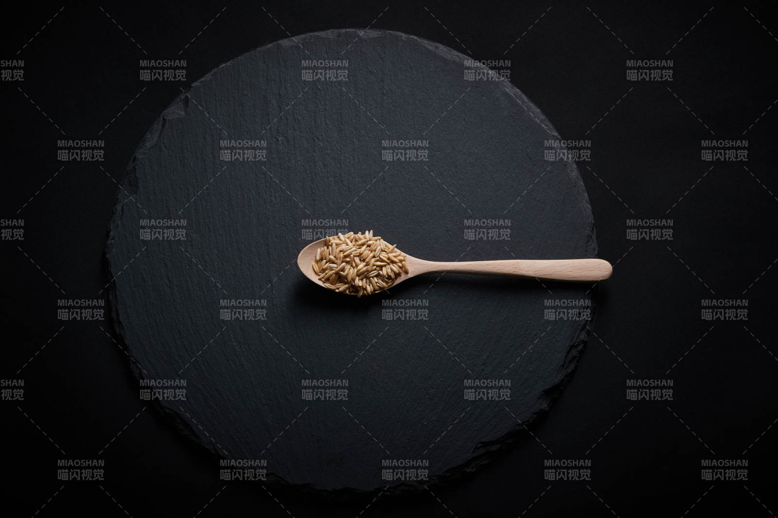 黑色青石板上的木质勺子装的燕麦米摆放在黑色背景中图片