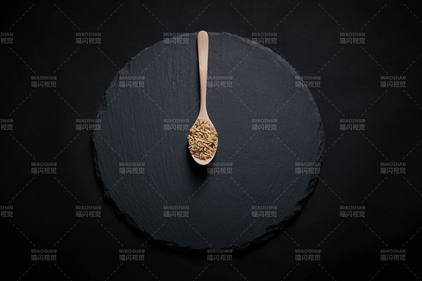 黑色青石板上的木质勺子装的燕麦米摆放在黑色背景中图片