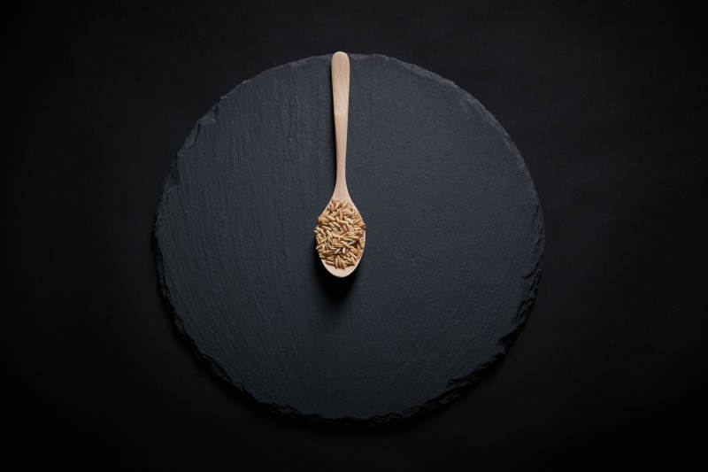 黑色青石板上的木质勺子装的燕麦米摆放在黑色背景中图片