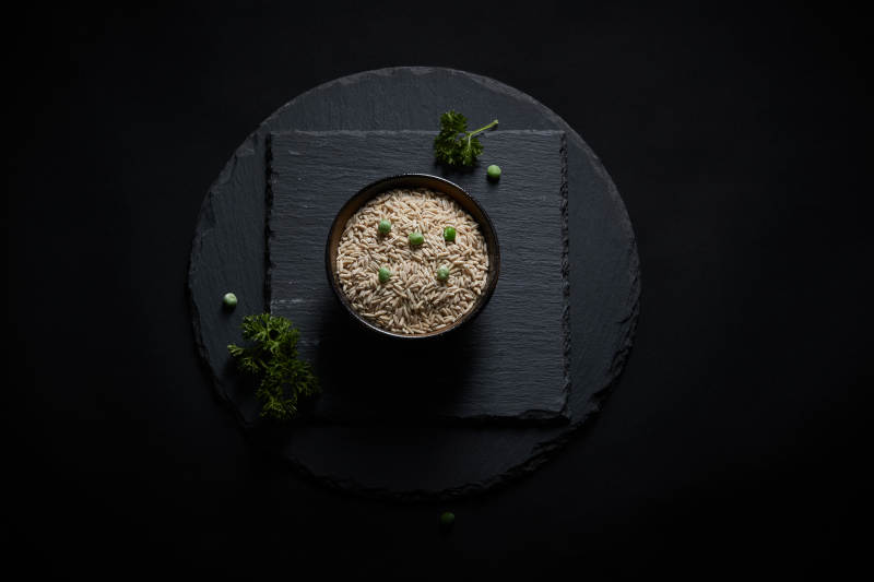 黑色青石板上的木质勺子装的燕麦米摆放在黑色背景中图片