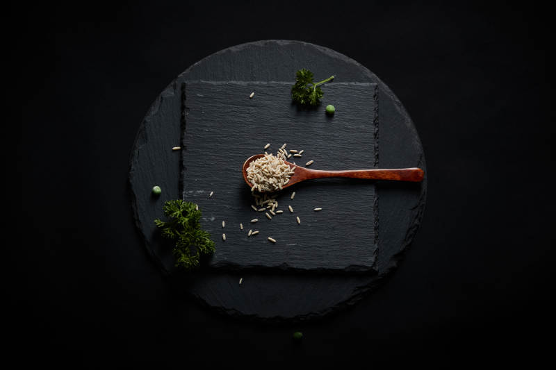 黑色青石板上的木质勺子装的燕麦米摆放在黑色背景中图片