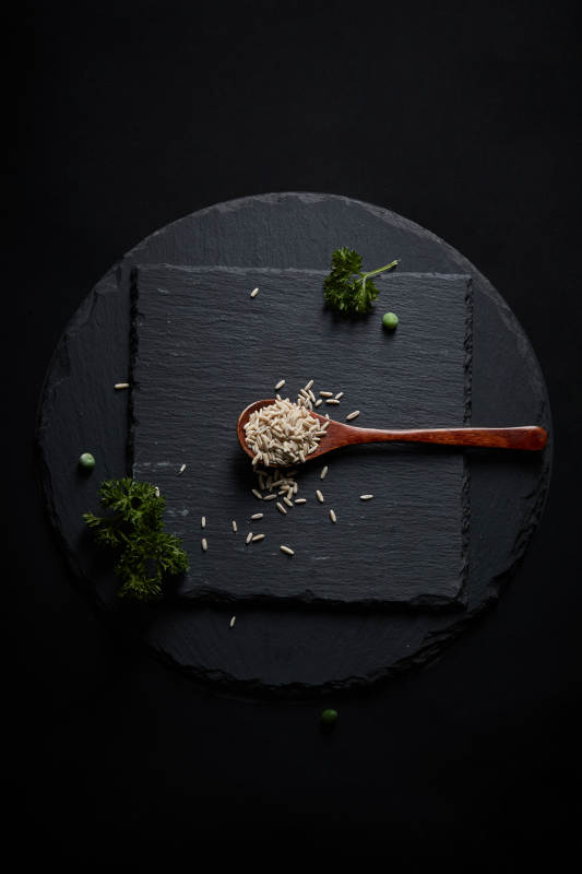 黑色青石板上的木质勺子装的燕麦米摆放在黑色背景中图片