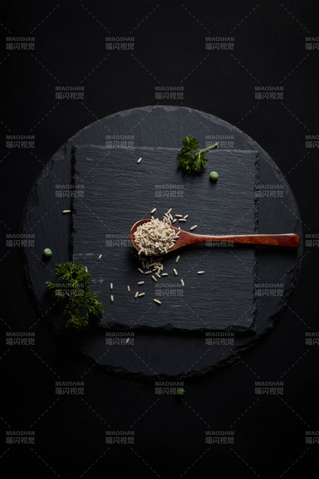 黑色青石板上的木质勺子装的燕麦米摆放在黑色背景中图片