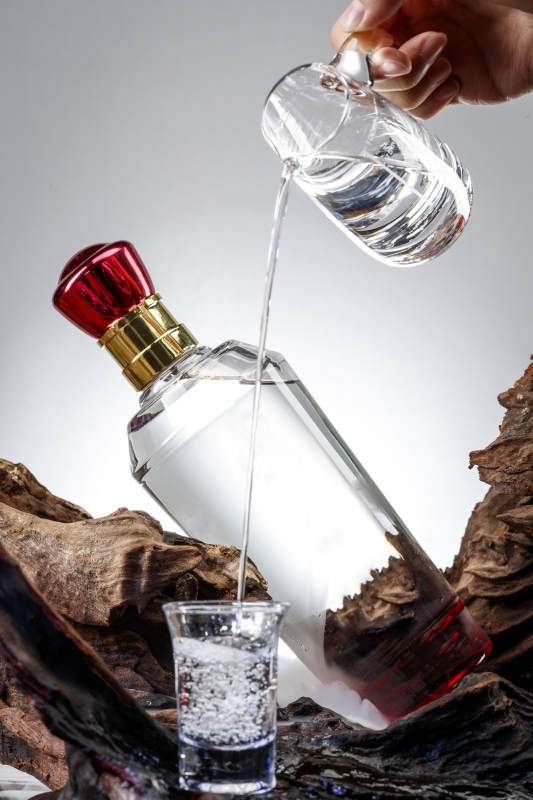 向木板上摆放的酒具内倒入清澈的白酒激起无数酒花图片