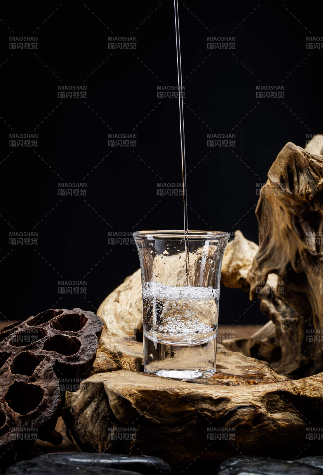 向木板上摆放的酒具内倒入清澈的白酒激起无数酒花图片