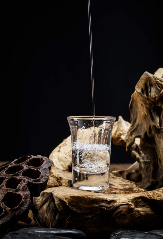 向木板上摆放的酒具内倒入清澈的白酒激起无数酒花图片