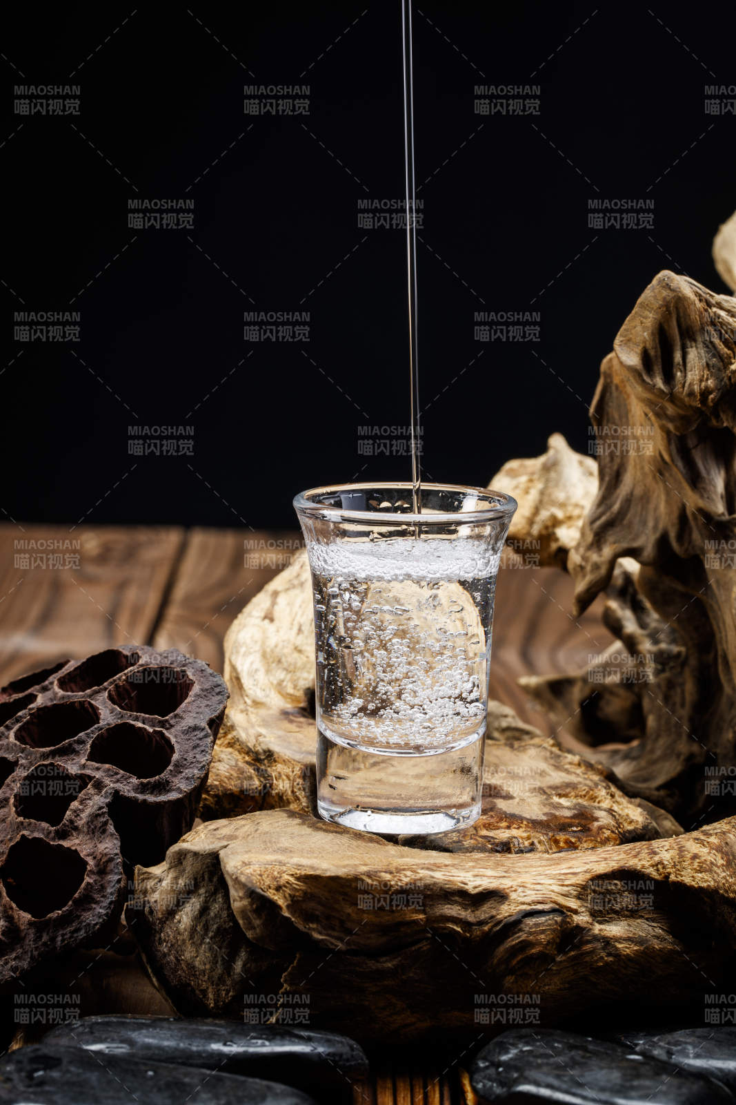 向木板上摆放的酒具内倒入清澈的白酒激起无数酒花图片