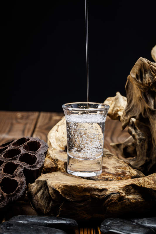 向木板上摆放的酒具内倒入清澈的白酒激起无数酒花图片