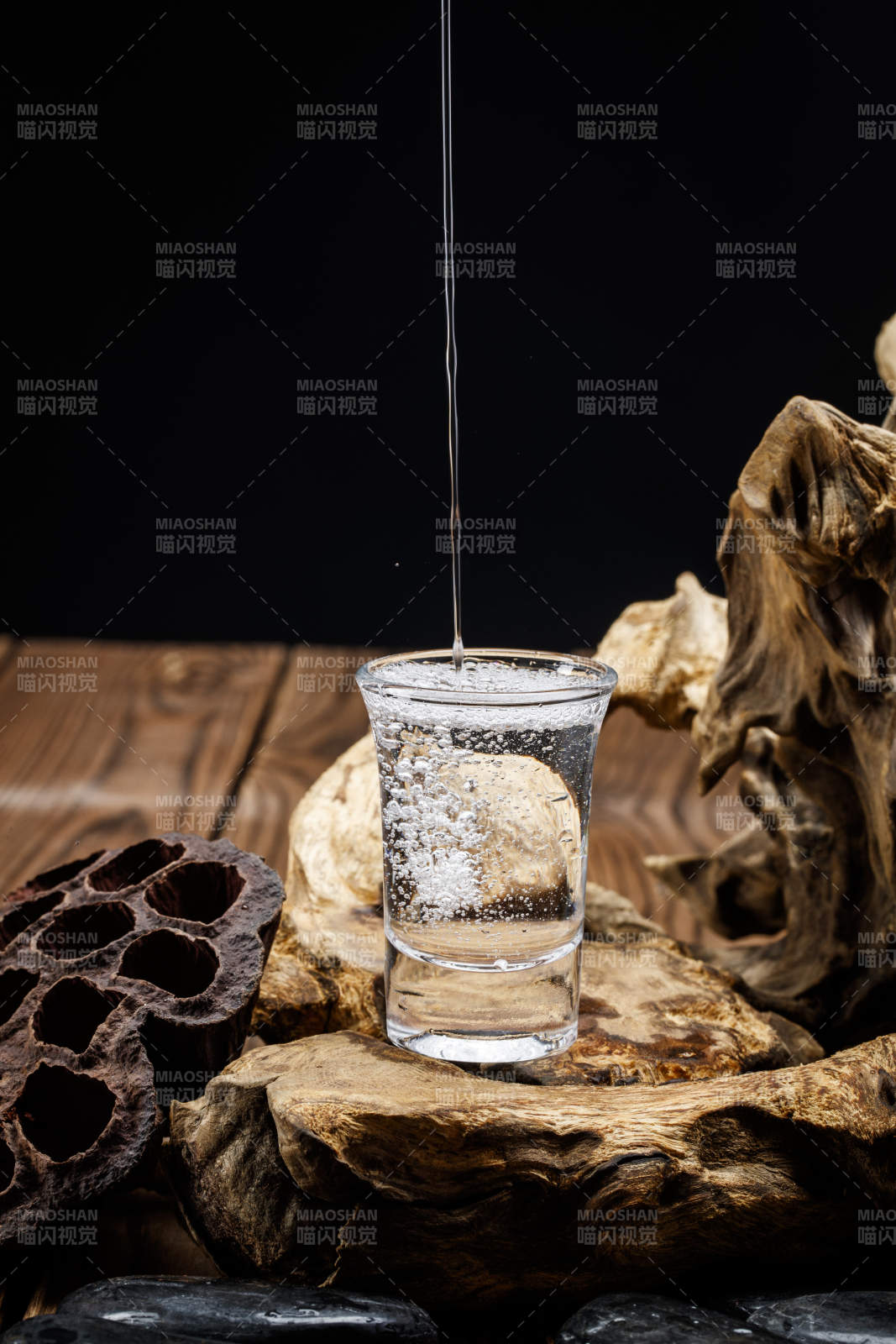 向木板上摆放的酒具内倒入清澈的白酒激起无数酒花图片