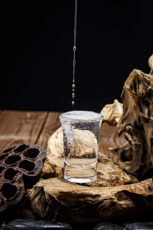 向木板上摆放的酒具内倒入清澈的白酒激起无数酒花图片