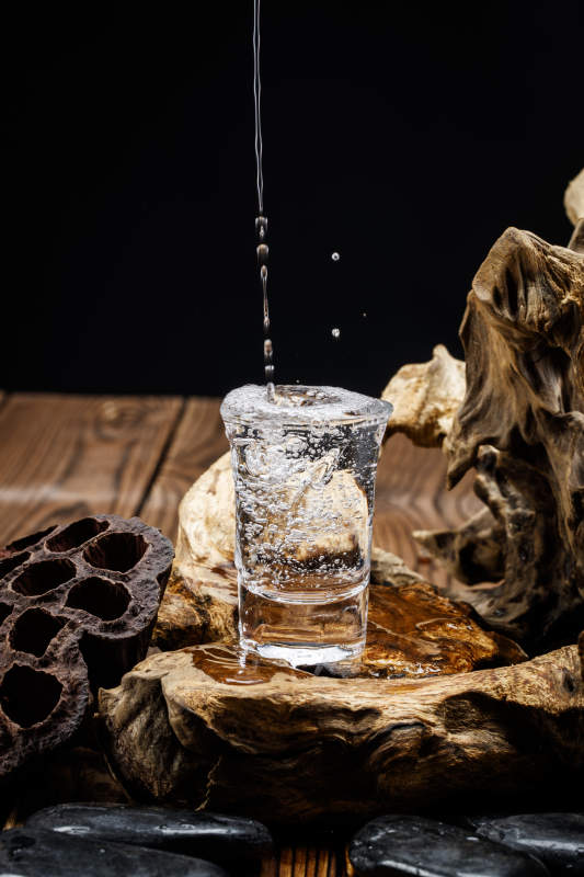 向木板上摆放的酒具内倒入清澈的白酒激起无数酒花图片