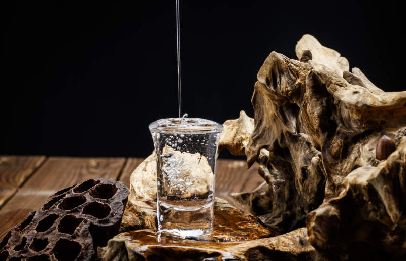 向木板上摆放的酒具内倒入清澈的白酒激起无数酒花图片