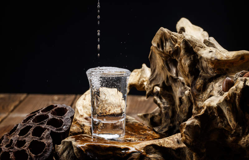 向木板上摆放的酒具内倒入清澈的白酒激起无数酒花图片