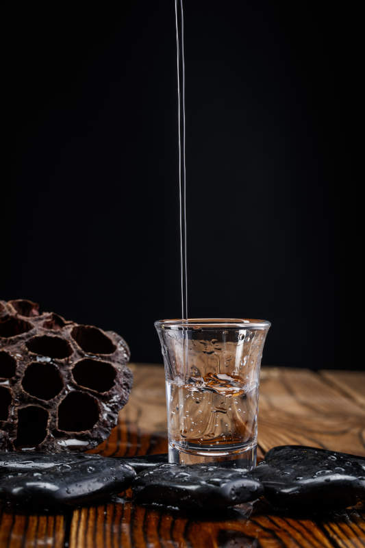 向木板上摆放的酒具内倒入清澈的白酒激起无数酒花图片