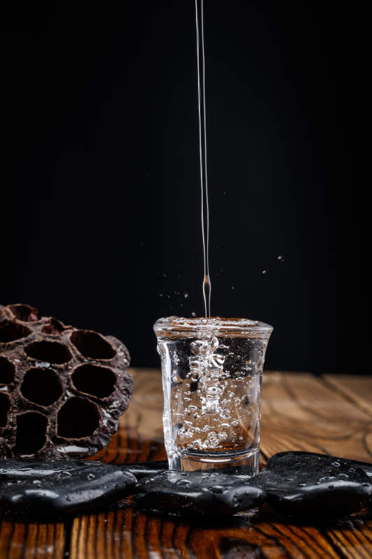 向木板上摆放的酒具内倒入清澈的白酒激起无数酒花图片