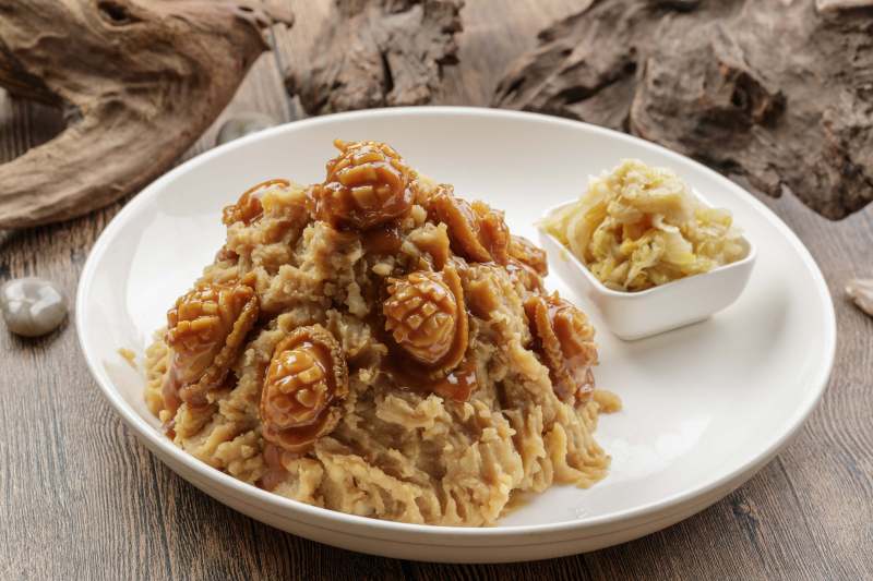 白色圆盘装的土豆焖鲍鱼摆放在樟木砧板上图片