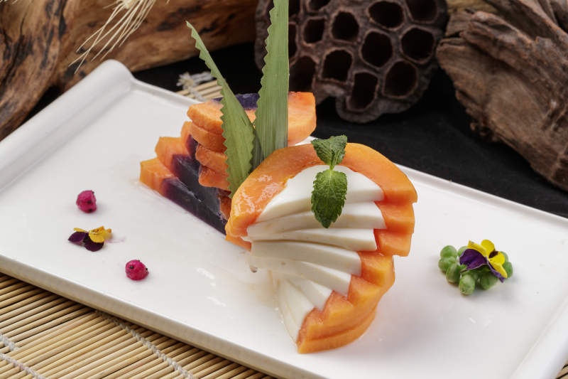 长方形瓷盘装的木瓜蛋白摆放在寿司帘上图片