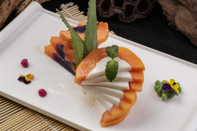 长方形瓷盘装的木瓜蛋白摆放在寿司帘上图片