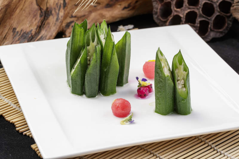 长方形瓷盘装的鲜秋葵摆放在寿司帘上图片