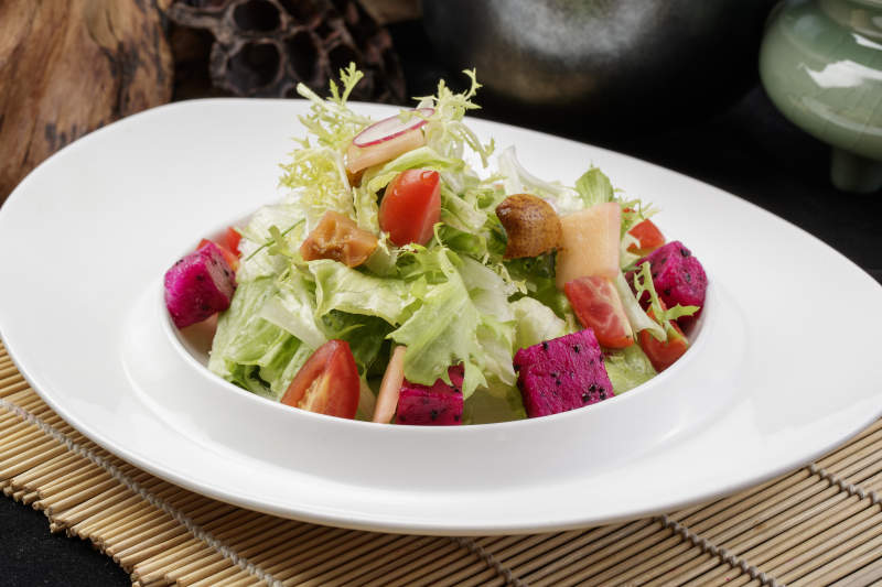 托圆瓷盘装的果蔬拌菜摆放在寿司帘上图片