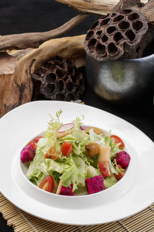 托圆瓷盘装的果蔬拌菜摆放在寿司帘上图片