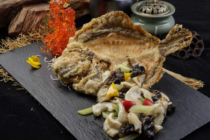 黑色石板装的两吃香酥多宝鱼摆放在黑色背景上图片