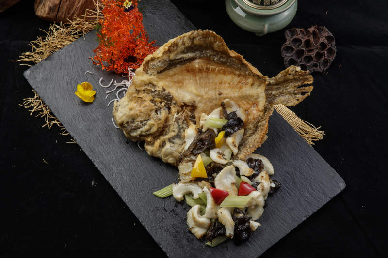 黑色石板装的两吃香酥多宝鱼摆放在黑色背景上图片