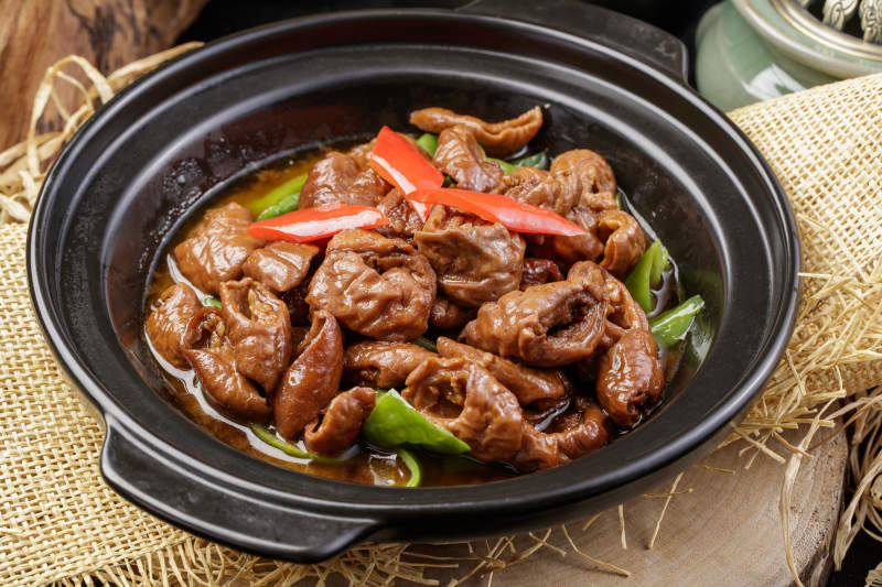 黑色砂锅装的砂锅肥肠摆放在麻布垫子上图片