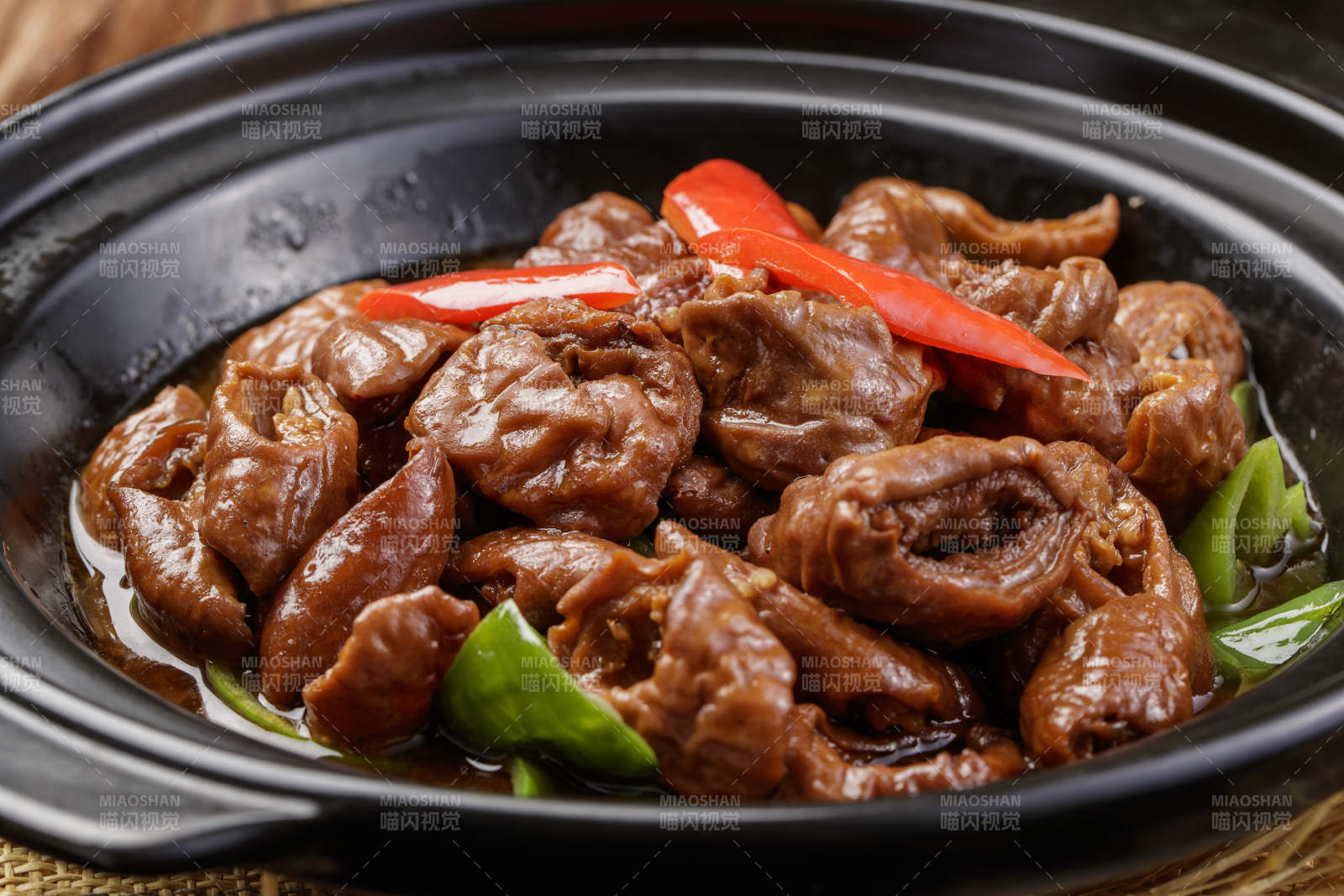 黑色砂锅装的砂锅肥肠摆放在麻布垫子上图片