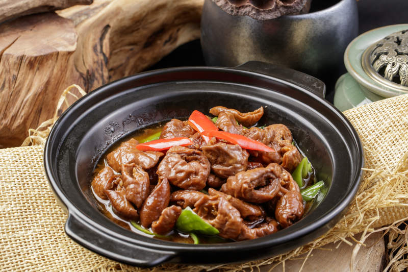 黑色砂锅装的砂锅肥肠摆放在麻布垫子上图片